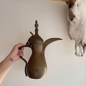 May include: A vintage brass coffee pot with a long spout and a decorative handle. The pot has a traditional Arabic design and is in good condition.