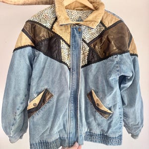May include: A multi-textured jacket featuring light blue denim panels, tan corduroy accents, and brown satin sections. The garment includes a tan corduroy collar, black lace trim, and a leopard print fabric panel. It has two front pockets with flaps.