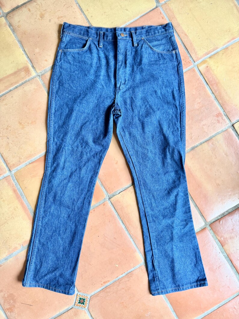 K&ouml;nnte beinhalten: Eine blaue Jeanshose mit klassischem F&uuml;nf-Taschen-Design. Die Jeans hat einen Knopf- und Rei&szlig;verschluss sowie einen leichten Schlag am Beinabschluss. Die Jeans ist aus einem mittelblauen Denim-Stoff gefertigt.