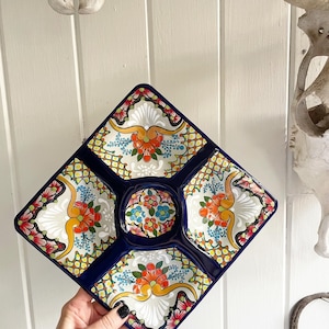May include: A square ceramic serving dish with five compartments. The dish is decorated with a colorful floral pattern in shades of blue, yellow, orange, and red. The dish has a dark blue border.