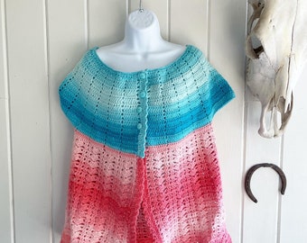 May include: A crocheted cardigan with a blue and pink ombre design. The cardigan has a button closure and short sleeves.