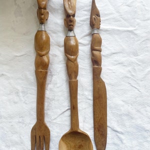 May include: A set of three wooden utensils with carved human figures. The utensils include a fork, a spoon, and a knife.