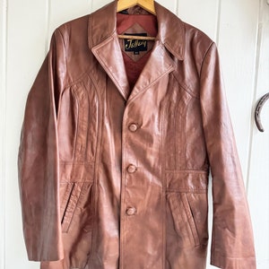 May include: A brown leather jacket with a button closure and a label that reads "Jellery 42".