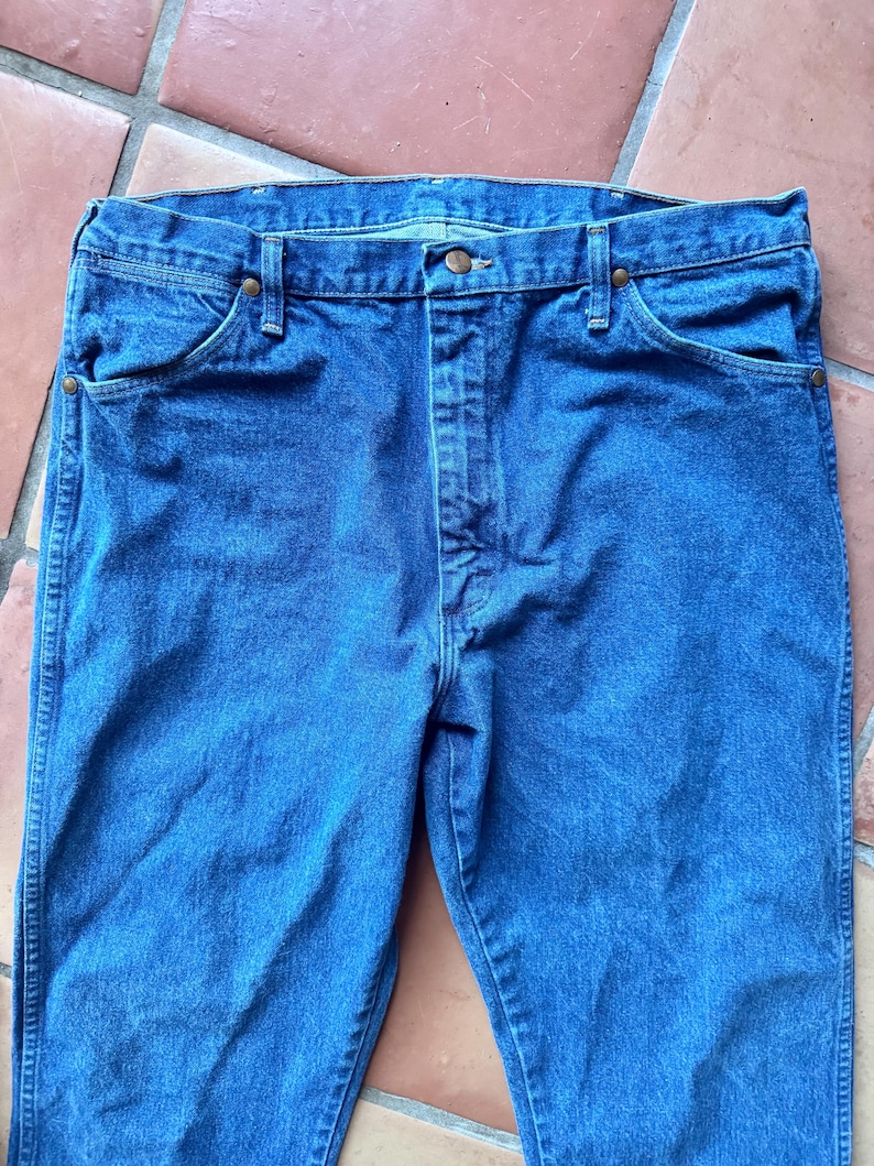 Puede incluir: Unos vaqueros de mezclilla azul de lavado medio con un dise&ntilde;o cl&aacute;sico de cinco bolsillos, cierre de botones y remaches met&aacute;licos de color cobre en las esquinas de los bolsillos. Los vaqueros tienen una cintura est&aacute;ndar con trabillas.