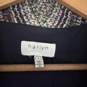 May include: Close-up of a jacket label with the brand name "harlyn" in white on a black background. The jacket's collar is visible, featuring a colorful woven pattern. The label also indicates the size is small and the jacket was made in China.
