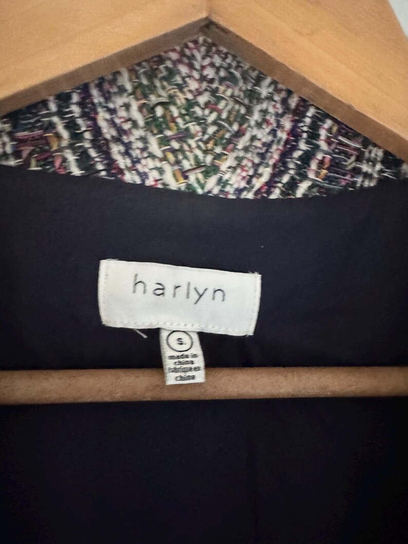 May include: Close-up of a jacket label with the brand name "harlyn" in white on a black background. The jacket's collar is visible, featuring a colorful woven pattern. The label also indicates the size is small and the jacket was made in China.