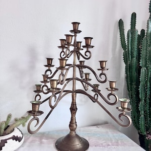 May include: A vintage brass candelabra with multiple candle holders. The candelabra has a central stem and curved arms, each holding a candle cup. The design features decorative swirls and a round base. The brass has a warm, aged patina.