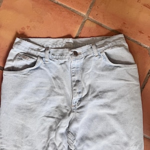 May include: Light blue denim jeans with a button closure and classic five-pocket design. The jeans are made of a light-wash denim fabric and have a straight leg cut. The jeans are shown on a terracotta tile surface.
