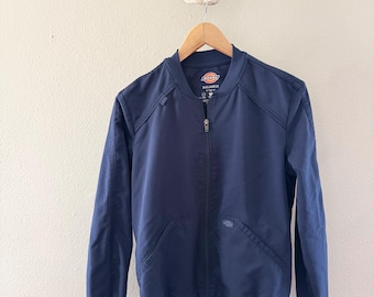 May include: A navy blue bomber jacket with a zipper closure and a Dickies logo on the left chest. The jacket has a ribbed collar, cuffs, and hem.