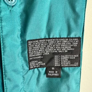 May include: Close-up of a teal jacket interior with a label indicating size 14 and "Made in Philippines." The label also lists fabric composition and care instructions. Teal buttons are visible.