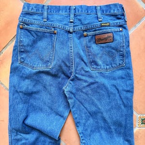 Puede incluir: Vaqueros azules de mezclilla con el logo de Wrangler en el bolsillo trasero. Los vaqueros tienen un dise&ntilde;o cl&aacute;sico de cinco bolsillos con pernera recta. Los bolsillos traseros presentan las costuras Wrangler. Los vaqueros est&aacute;n hechos de mezclilla duradera.