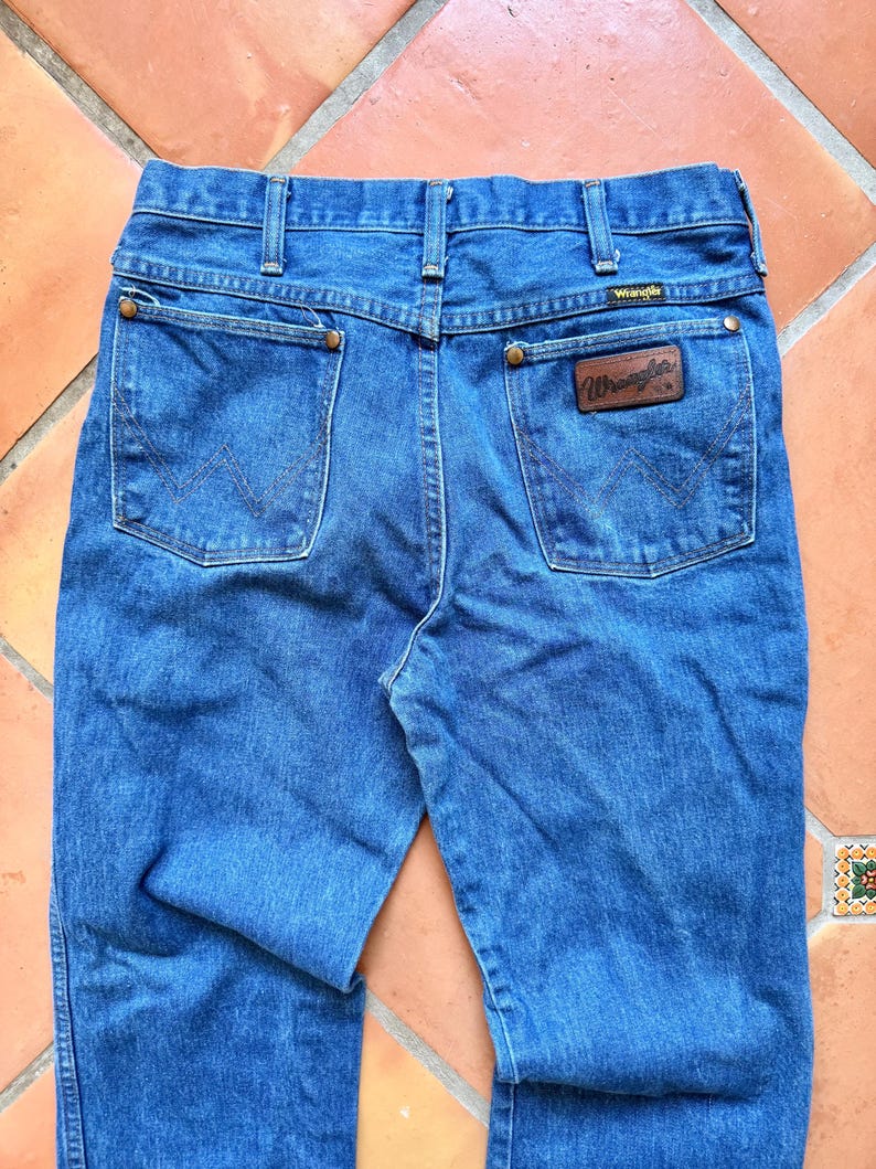Puede incluir: Vaqueros azules de mezclilla con el logo de Wrangler en el bolsillo trasero. Los vaqueros tienen un dise&ntilde;o cl&aacute;sico de cinco bolsillos con pernera recta. Los bolsillos traseros presentan las costuras Wrangler. Los vaqueros est&aacute;n hechos de mezclilla duradera.