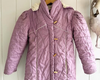 May include: A purple quilted jacket with a white trim and wooden button closures. The jacket has a hood and a drawstring at the waist.