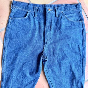 K&ouml;nnte beinhalten: Nahaufnahme einer blauen Jeans. Die Jeans hat ein klassisches F&uuml;nf-Taschen-Design, einen Knopf- und Rei&szlig;verschluss sowie G&uuml;rtelschlaufen. Der Denim hat ein leicht verwaschenes Aussehen.