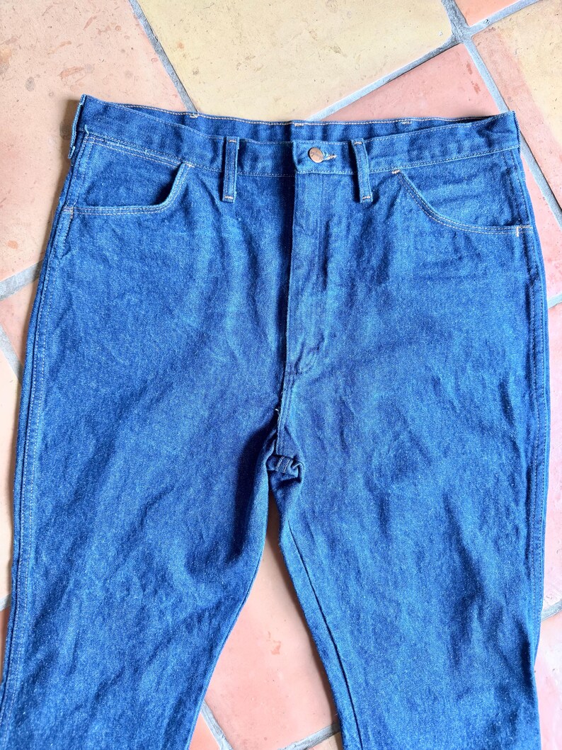 K&ouml;nnte beinhalten: Nahaufnahme einer blauen Jeans. Die Jeans hat ein klassisches F&uuml;nf-Taschen-Design, einen Knopf- und Rei&szlig;verschluss sowie G&uuml;rtelschlaufen. Der Denim hat ein leicht verwaschenes Aussehen.