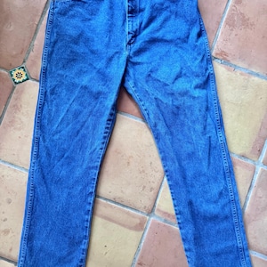 May include: A pair of medium-wash blue denim jeans featuring a classic five-pocket design, a button fly closure, and copper-toned rivets at the pocket corners. The jeans have a straight-leg cut with visible stitching along the seams and waistband.