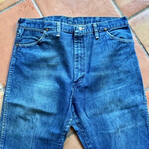 May include: Close-up of blue denim jeans. The jeans have a button closure and pockets. The denim has a faded appearance, with lighter areas on the thighs and knees. The jeans are a classic style.