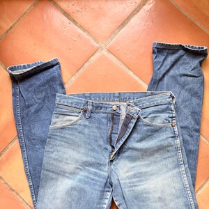 K&ouml;nnte beinhalten: Hellblaue Jeans aus Denim mit klassischem F&uuml;nf-Taschen-Design. Die Jeans liegen flach, wobei die Vorderseite mit teilweise ge&ouml;ffnetem Rei&szlig;verschluss zu sehen ist. Der Stoff hat ein verwaschenes Aussehen.