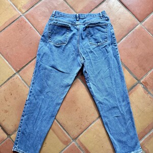 May include: Light blue denim jeans with a classic five-pocket design. The jeans are laid flat, showcasing the back pockets and the overall shape. The fabric has a slightly faded appearance, suggesting a vintage or worn look.
