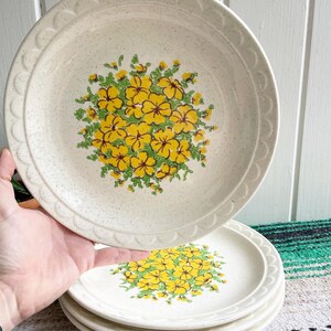May include: Set of four white ceramic dinner plates with a yellow and green floral design. The plates have a speckled finish and a scalloped edge.