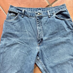 May include: Light blue denim jeans with a button closure and front and back pockets. The jeans have a classic five-pocket design and a straight leg fit. The Calvin Klein logo is visible on the front pocket.