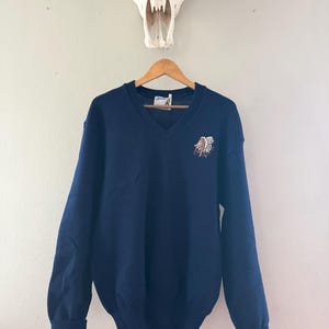 May include: A navy blue v-neck sweater with a Native American headdress embroidered on the front.