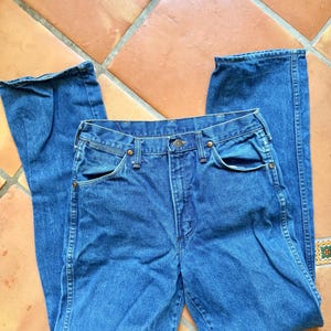 Puede incluir: Vaqueros de mezclilla azules con un dise&ntilde;o cl&aacute;sico de cinco bolsillos. Los vaqueros tienen cierre de bot&oacute;n y cremallera, con remaches color cobre y una pernera recta. La tela parece ser una mezclilla de lavado medio.
