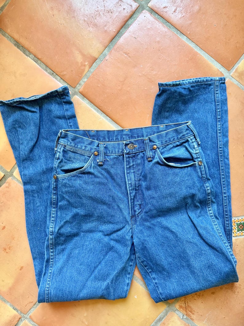 Puede incluir: Vaqueros de mezclilla azules con un dise&ntilde;o cl&aacute;sico de cinco bolsillos. Los vaqueros tienen cierre de bot&oacute;n y cremallera, con remaches color cobre y una pernera recta. La tela parece ser una mezclilla de lavado medio.