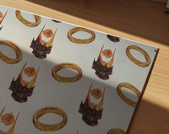 May include: A light gray sheet of paper featuring a repeating pattern of golden rings and dark, jagged tower structures topped with glowing orange flames. The design is printed across the surface in a consistent, alternating grid layout.