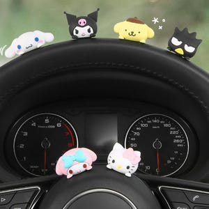 Könnte beinhalten: Ein schwarzes Armaturenbrett eines Autos mit einem Tachometer und Drehzahlmesser. Mehrere kleine, bunte Figuren von Comicfiguren sind am Armaturenbrett befestigt.