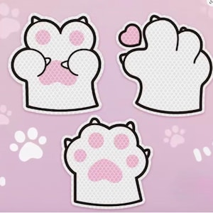 May include: Three white cat paw-shaped stickers with pink paw pads and black outlines. One paw has a heart. The stickers are on a light pink background with paw print accents. These stickers are perfect for decorating.