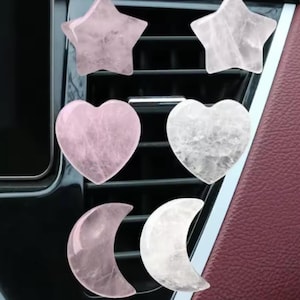 Może przedstawiać: Kolekcja dyfuzorów do wentylacji samochodowej z różowego kwarcu w kształcie gwiazd, serc i półksiężyców. Kryształy są w różnych odcieniach różu i bieli, z widocznymi naturalnymi teksturami. Tło obejmuje kratkę wentylacyjną samochodu i bordowe wnętrze.