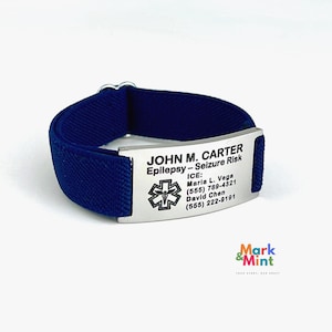 May include: A navy blue medical alert bracelet with a stainless steel plate. The plate is engraved with the name "JOHN M. CARTER", medical condition, and emergency contact information. The bracelet features a medical symbol.