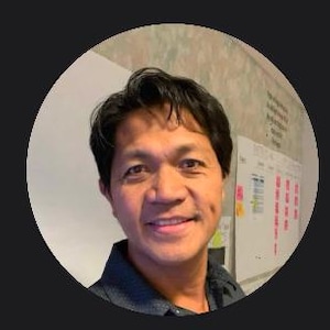 Può includere: Un uomo sorridente con capelli neri corti che indossa una camicia blu scuro con colletto.