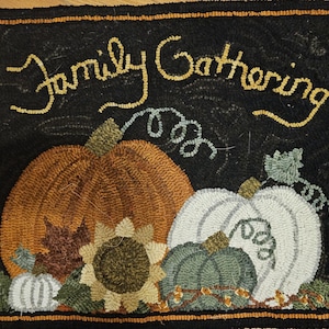 May include: A black rug with a fall theme, featuring the words "Family Gathering" in yellow. The rug depicts an orange pumpkin, a white pumpkin, a green pumpkin, and a sunflower. The rug is bordered with a brown and orange trim.
