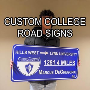 May include: A blue custom college road sign with white lettering. The sign reads "Hills West" to "Lynn University", "Fighting Knights", "1281.4 Miles", and "Marcus DeGregorio". The sign has a shield logo.