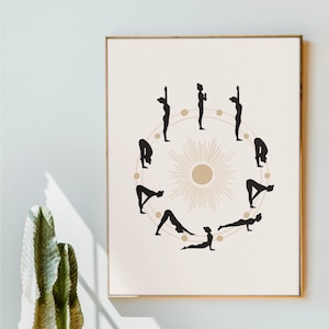 Op de afbeelding: Een ingelijste print met zwarte silhouetten van yogahoudingen in een cirkel. In het midden een zonmotief met een gouden cirkel. De achtergrond is neutraal beige.