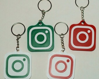 May include: Four keyrings featuring the Instagram logo in green, red, and white. Each keyring has a silver ring and chain. The Instagram logo is a square with a rounded corner design and a camera icon in the centre.