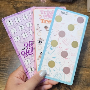 May include: Three colorful budget cards with Halloween themes. One card is purple with paw prints and the text "Ho Hall". Another is pink with the text "Trick or Treat". The third is light blue with the text "Save 55".