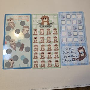 May include: Three colorful planner cards with otter illustrations. One card says "An otter day in paradise!" with scratch-off circles. Another says "Otter Nonsense" with otter images. The third says "Every Otter Day Is A New Adventure!"