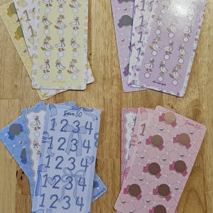 May include: A collection of decorative cards in various colors, including yellow, purple, blue, and pink. The cards feature illustrations of ducks, bows, and numbers. Some cards have the text "Save 50" and "Save 55".