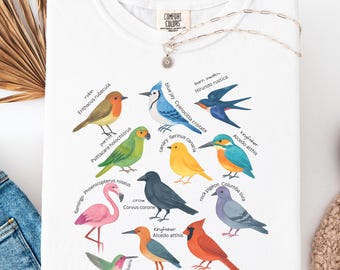 May include: White crew neck t-shirt featuring colorful illustrations of various bird species, including a blue jay, cardinal, and hummingbird. The shirt has the text "COMFORT COLORS" on the tag.