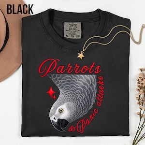 May include: Black t-shirt with a graphic of a gray parrot and the words "Parrots & Panic Attacks" in red script. A gold star pendant necklace and a Comfort Colors tag are visible.