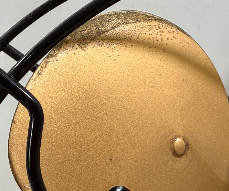 May include: Close-up of a football helmet. The helmet has a gold-coloured face mask and a black metal cage. The gold surface has a textured appearance with small, dark spots.