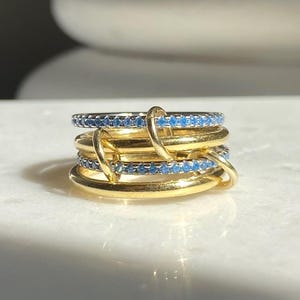 Może przedstawiać: Zestaw czterech złotych pierścionków z niebieskimi kamieniami szlachetnymi. Pierścionki są ułożone jeden na drugim i są przeznaczone do noszenia razem.