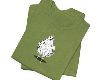 May include: Green t-shirt featuring a white ghost graphic with a black outline. The ghost is depicted with a smiling face and is dripping from the bottom. The t-shirt is folded and has a crew neck.