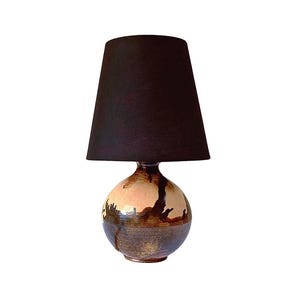 Könnte beinhalten: Eine Keramik-Tischlampe mit einem runden, braunen und beigefarbenen Sockel und einem schwarzen Stoffschirm.