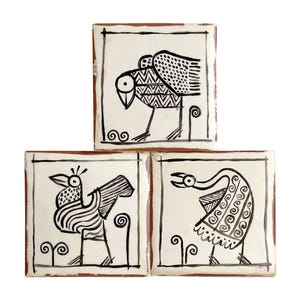 May include: Three square ceramic tiles featuring hand-painted black line art of stylized birds on a white background. Each tile displays a unique avian figure with geometric patterns, set within a thin black border and a terracotta-colored edge.