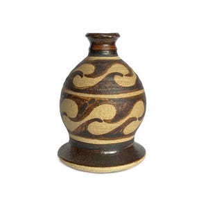 Puede incluir: Un jarrón de cerámica marrón con una base ancha y un cuello estrecho. El jarrón está decorado con un patrón de ondas marrones y beige.