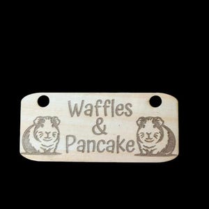 May include: A wooden sign with the text "Waffles & Pancake" and two cartoon guinea pigs on either side of the text.